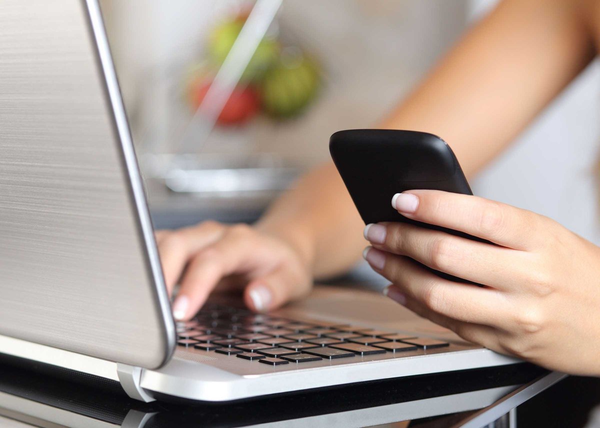 Woman hand using a smart phone and typing a laptop at home