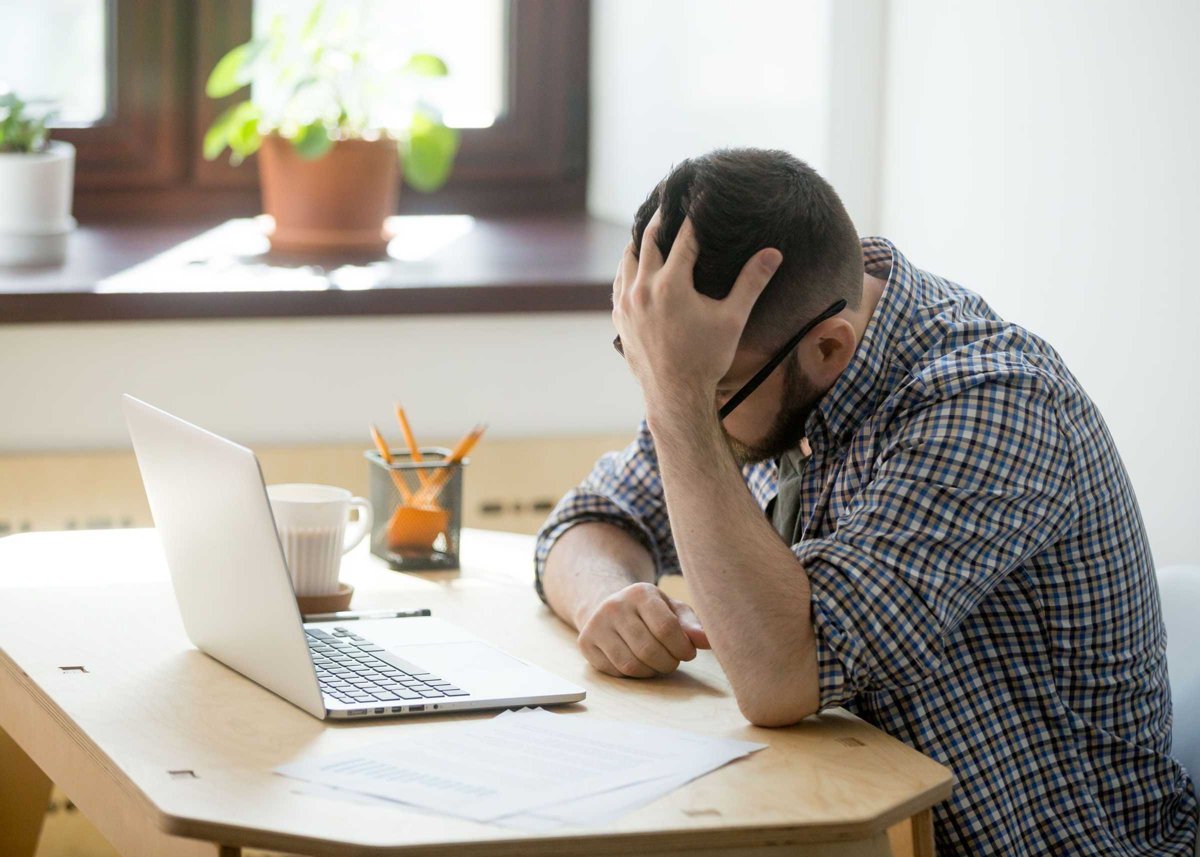 Depressed man looking in his laptop computer receiving bad news.