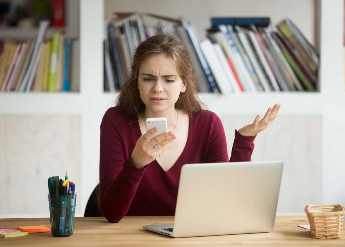 Frustrated female entrepreneur looking at cellphone and shruggin