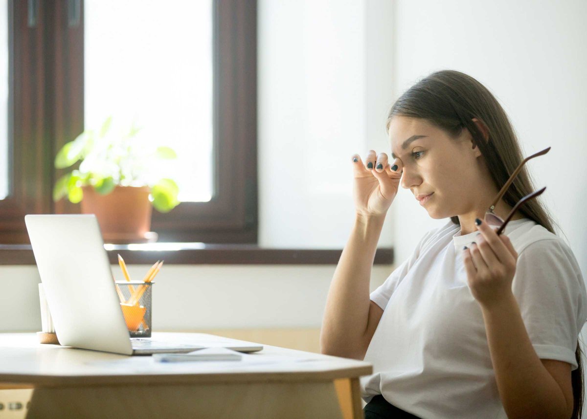 Tired businesswoman holding glasses and rubbing eyes in home off
