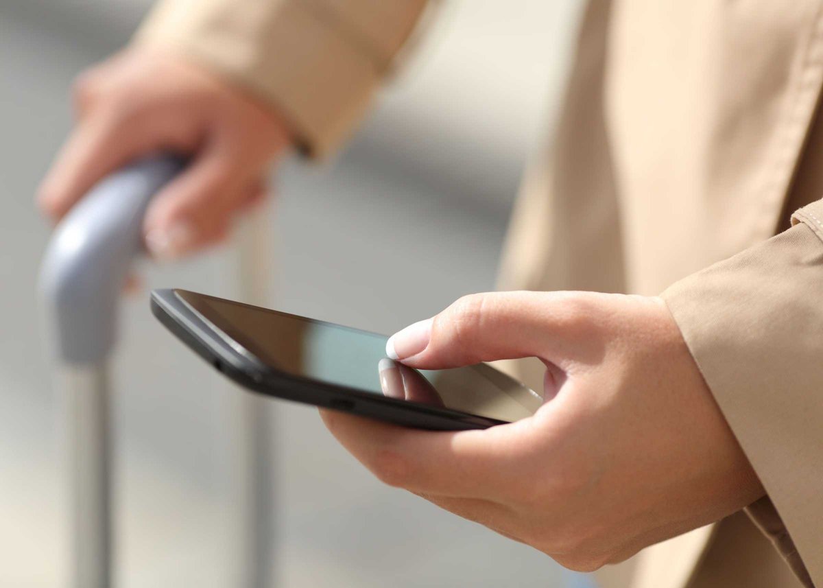 Traveler woman hand consulting a smartphone and holding a suit case