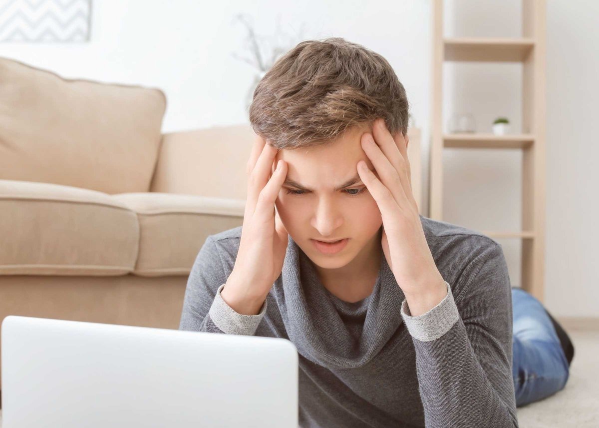 Depressed teenager using laptop on floor in room