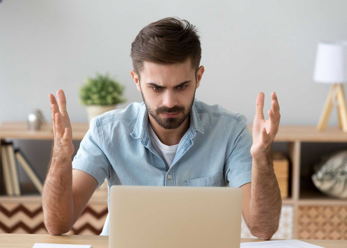 Irritated man looking at laptop screen sitting at the desk