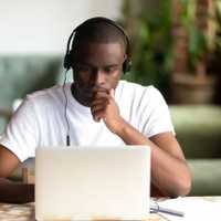 Focused African American man wear headphones, using laptop