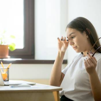 Tired businesswoman holding glasses and rubbing eyes in home off