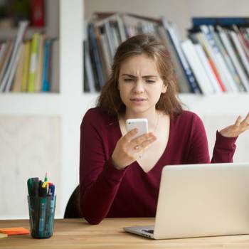 Frustrated female entrepreneur looking at cellphone and shruggin