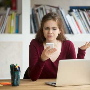 Frustrated female entrepreneur looking at cellphone and shruggin