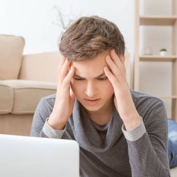 Depressed teenager using laptop on floor in room