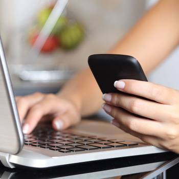 Woman hand using a smart phone and typing a laptop at home