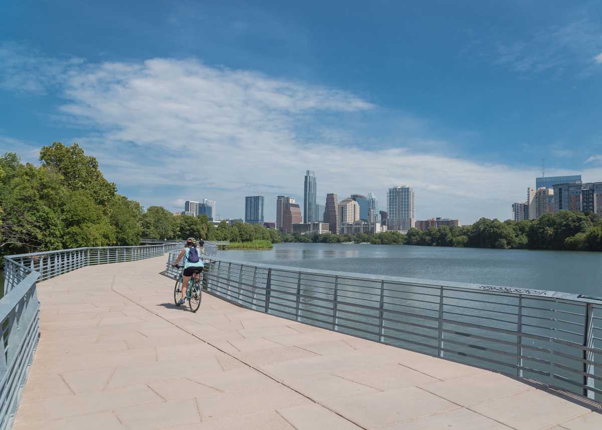 People biking running walking along Colorado River waterfront boardwalk near downtown Austin, Texas in summer day
